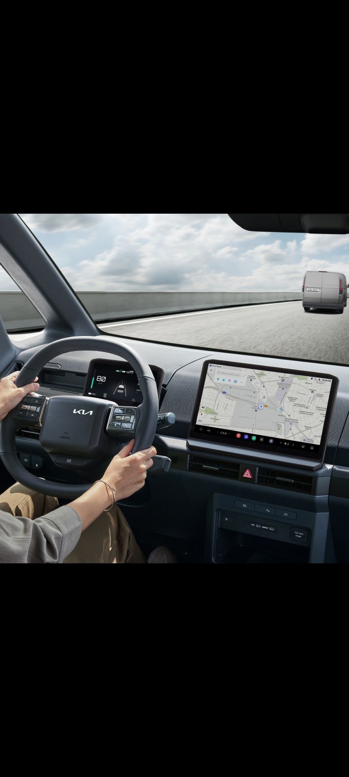 Fahrer hält das Lenkrad des Kia PV5 Cargo. Das Navigations-Display ist gut sichtbar.